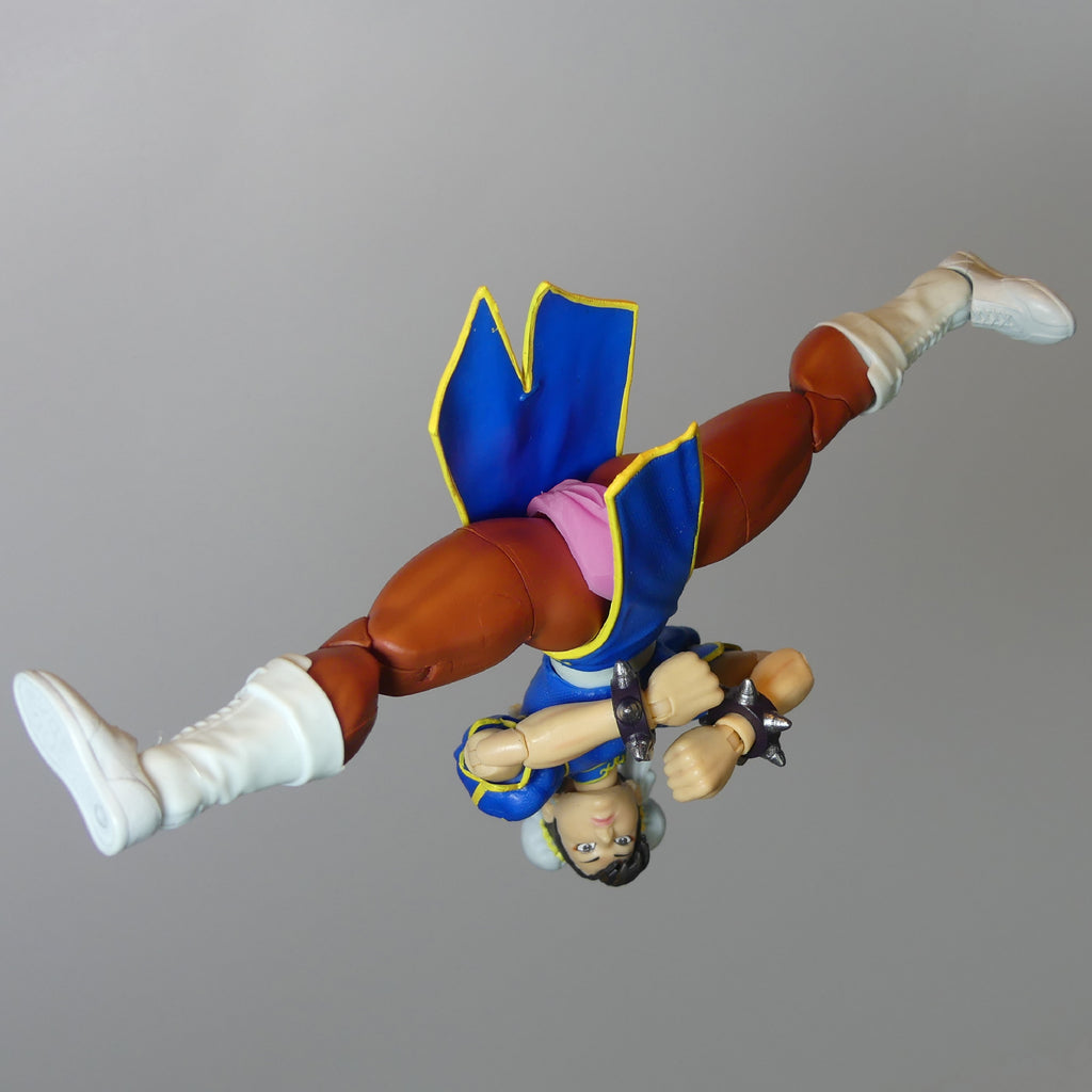 A Street Fighter figurine of Chun-Li shown upside down in a flying pose, wearing her signature blue outfit with a pink silicone vagina and white boots