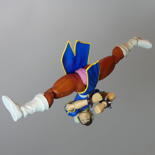 A Street Fighter figurine of Chun-Li shown upside down in a flying pose, wearing her signature blue outfit with a pink silicone vagina and white boots