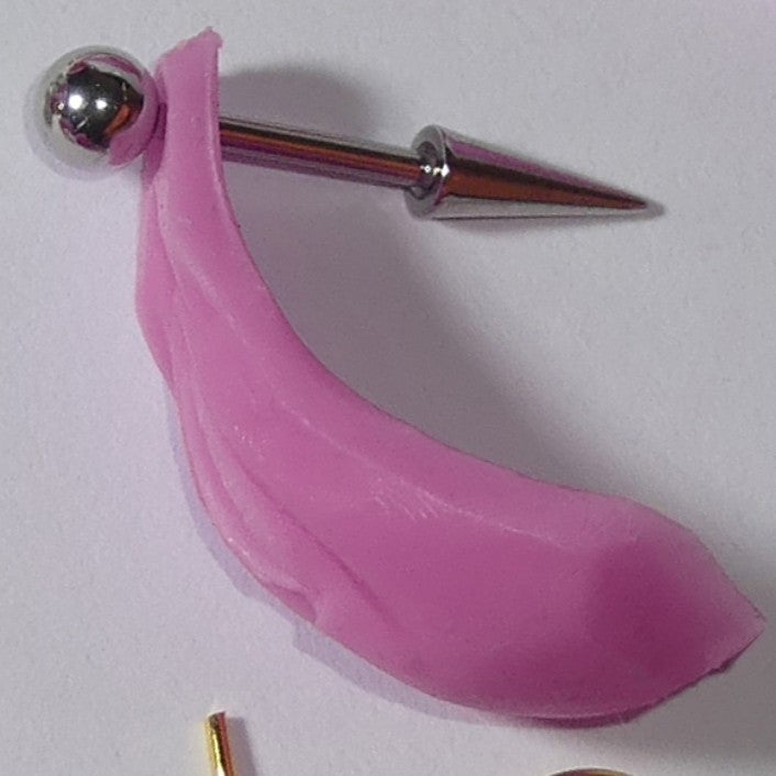 A pink silicone or rubber vagina accessory attached to a silver metal pin with a spherical end, photographed on a plain light background.