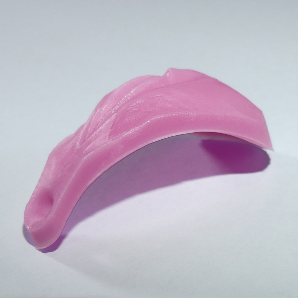 A pink, curved silicone accessory with a textured surface and a small anus at one end, shown on a plain light gray background.